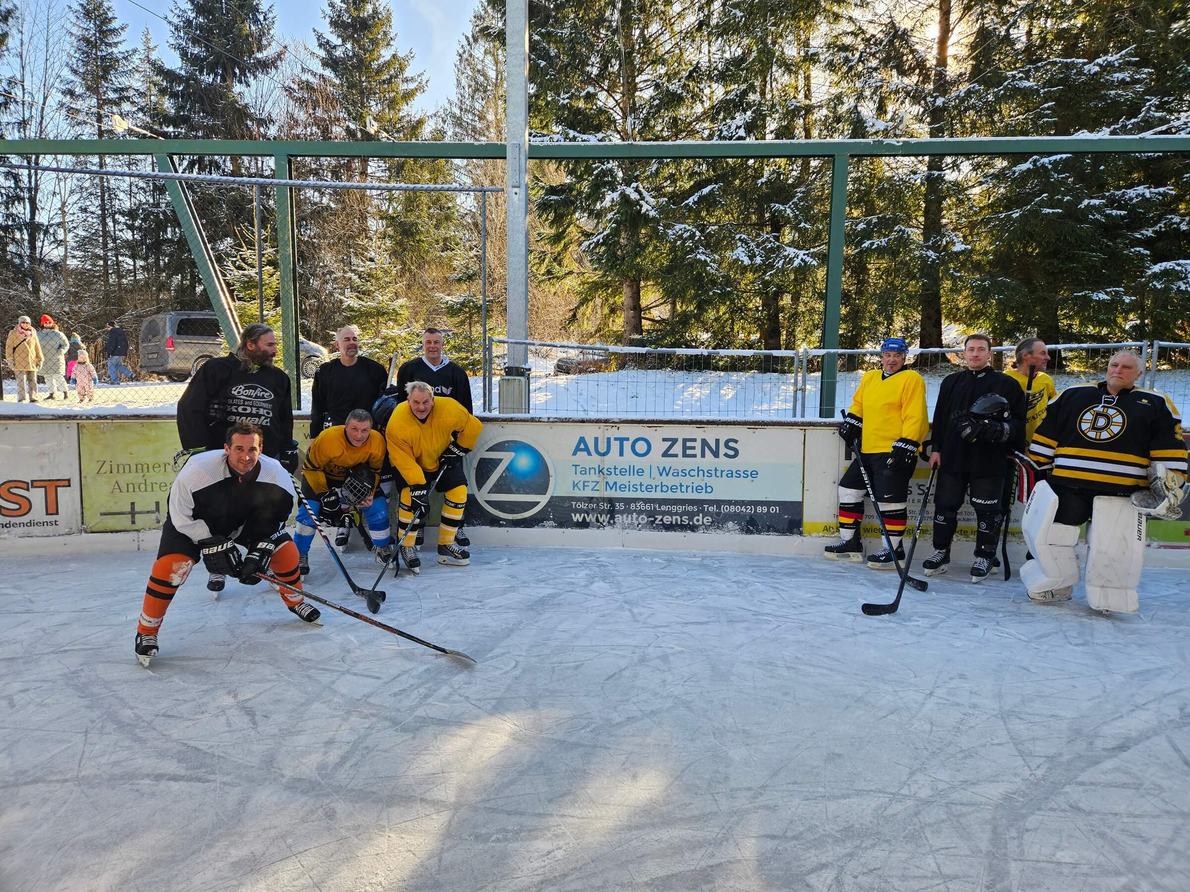 Eishockeyteam auf einer verschneiten Outdoor-Eisbahn in Langgries, Gruppenfoto vor Werbebanden von lokalen Unternehmen. Bild: Eishockeyspieler auf einer Outdoor-Eisbahn vor Werbebanden im Winter, bereit für das Spiel.